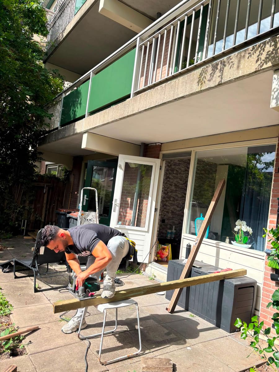 Timmerman zaagt een tuinbalk op maat met een cirkelzaag, naast de woning waar de berging komt