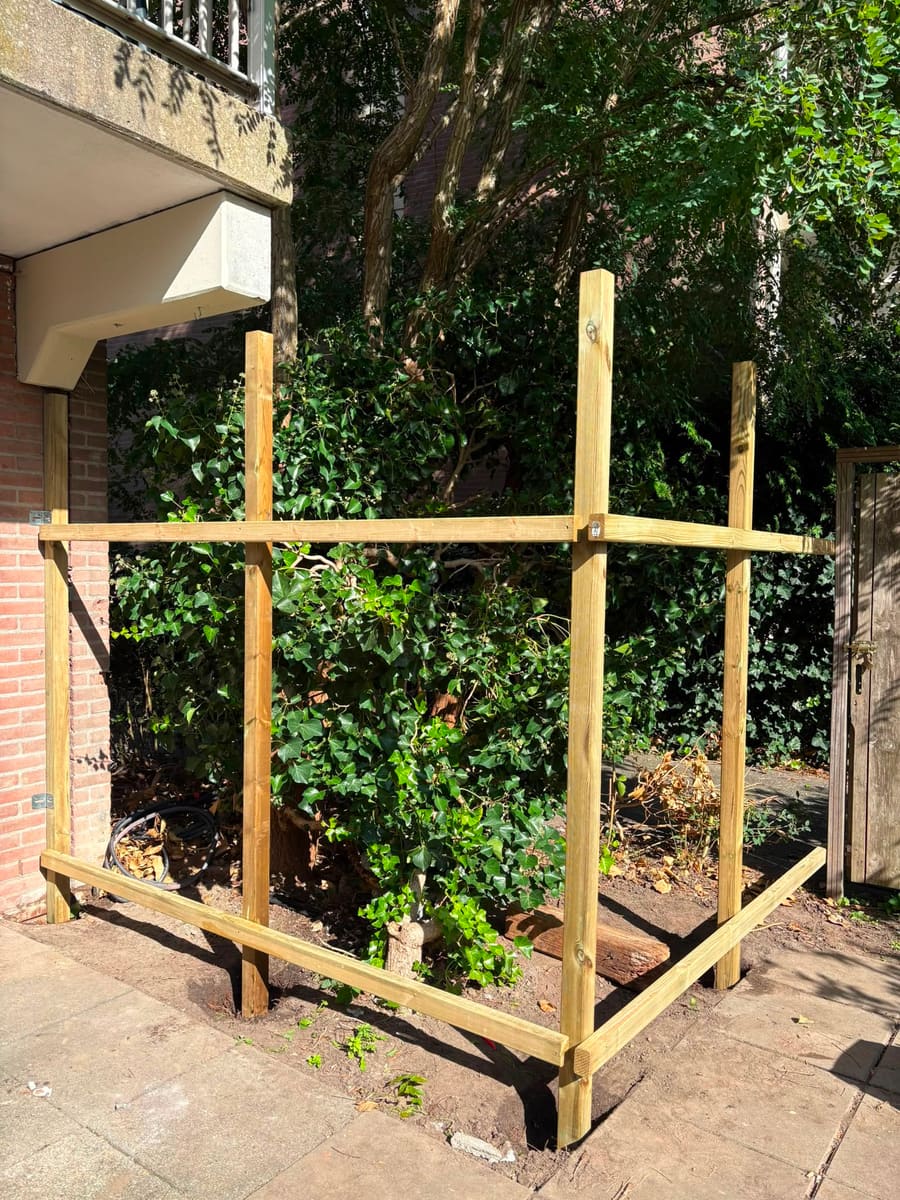 Staand houten frame van een berging, met staanders en regels tegen de gevel gemonteerd