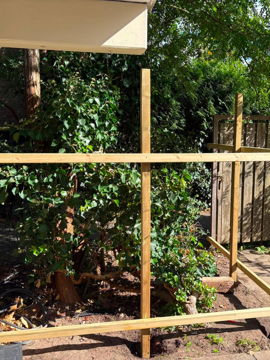 Het houten frame van de berging gezien vanuit de tuin, met de gevel en de bestaande poort erachter