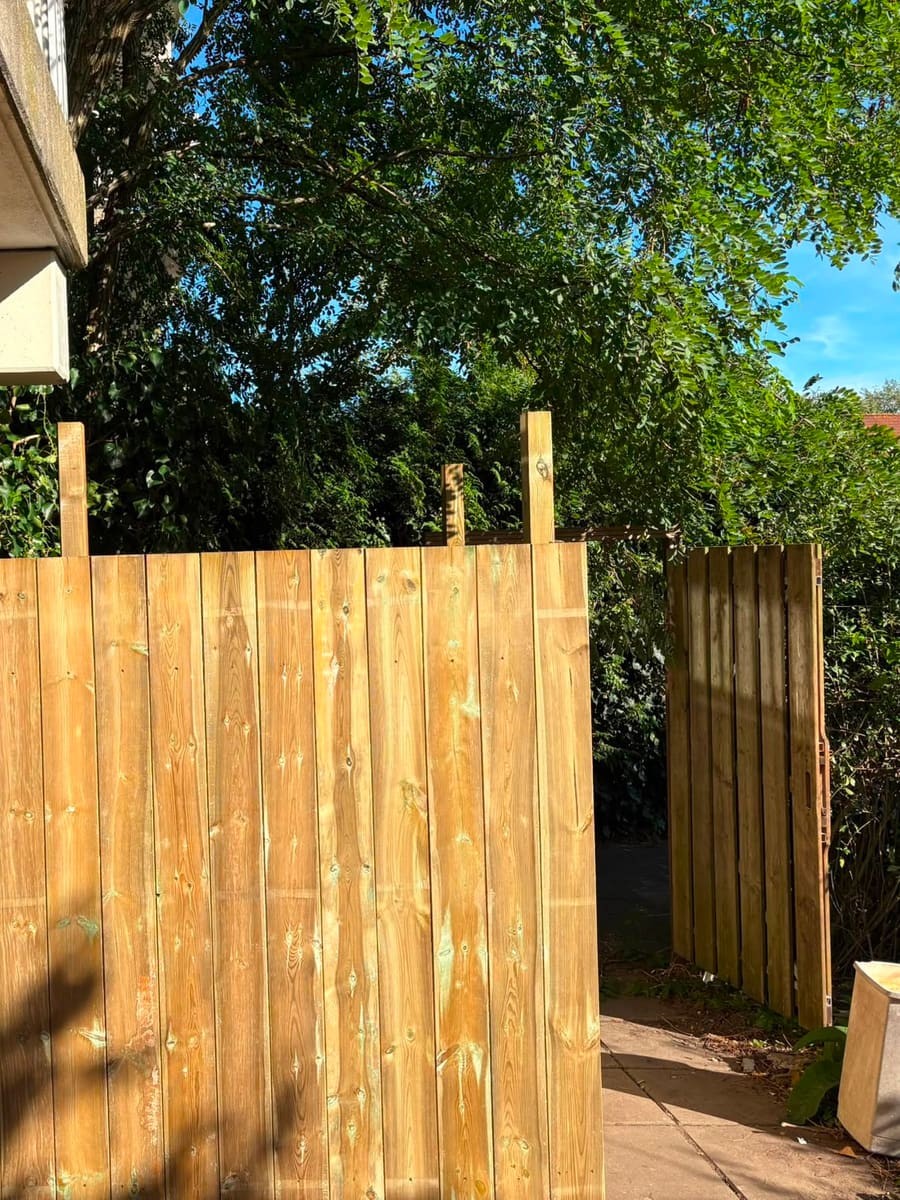 De berging met de schuttingplanken erop, met daarnaast de doorgang naar de tuinpoort